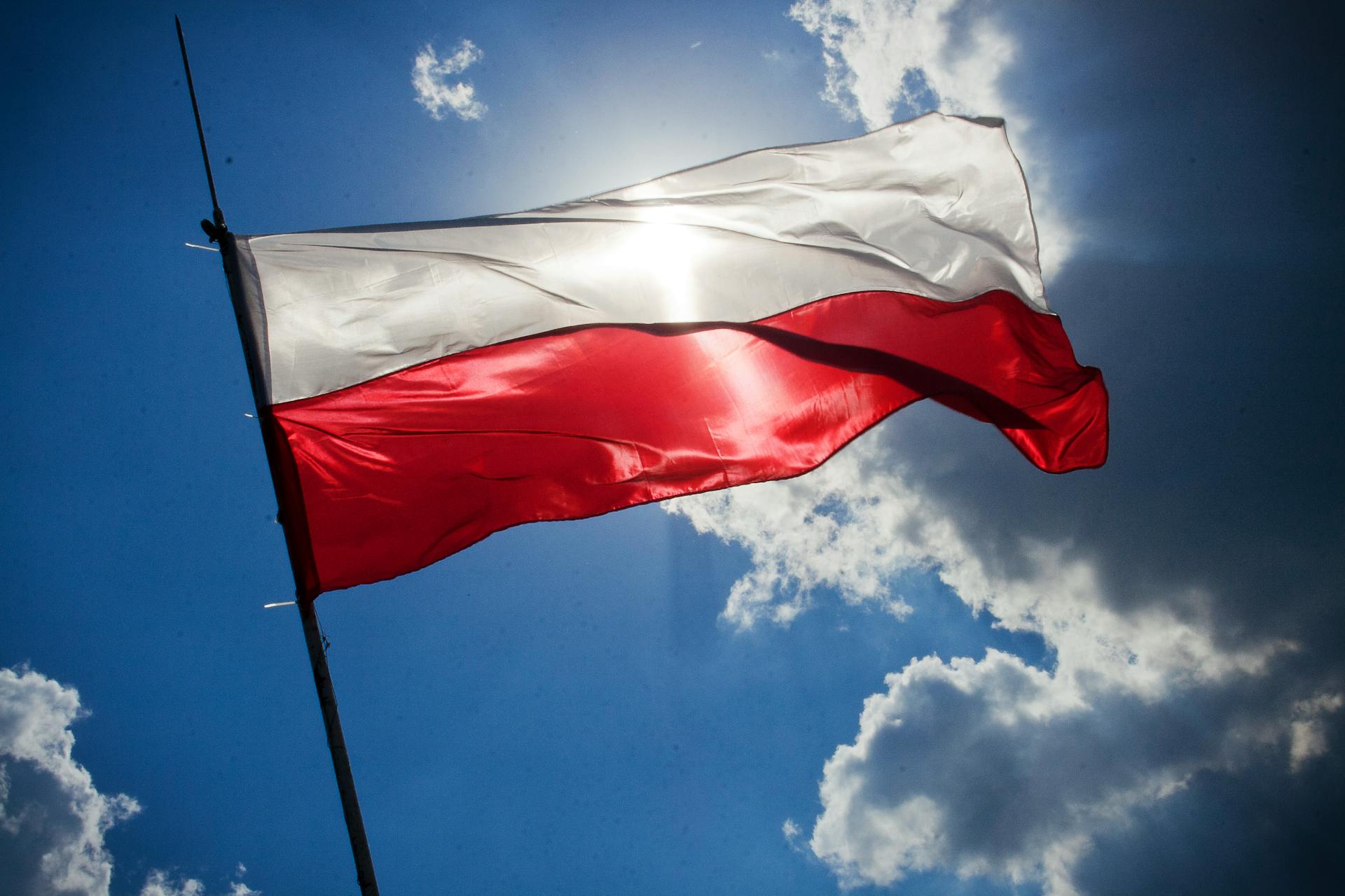 Flaga Polski (biało-czerwona) na tle błękitnego nieba i niewielkich chmur.